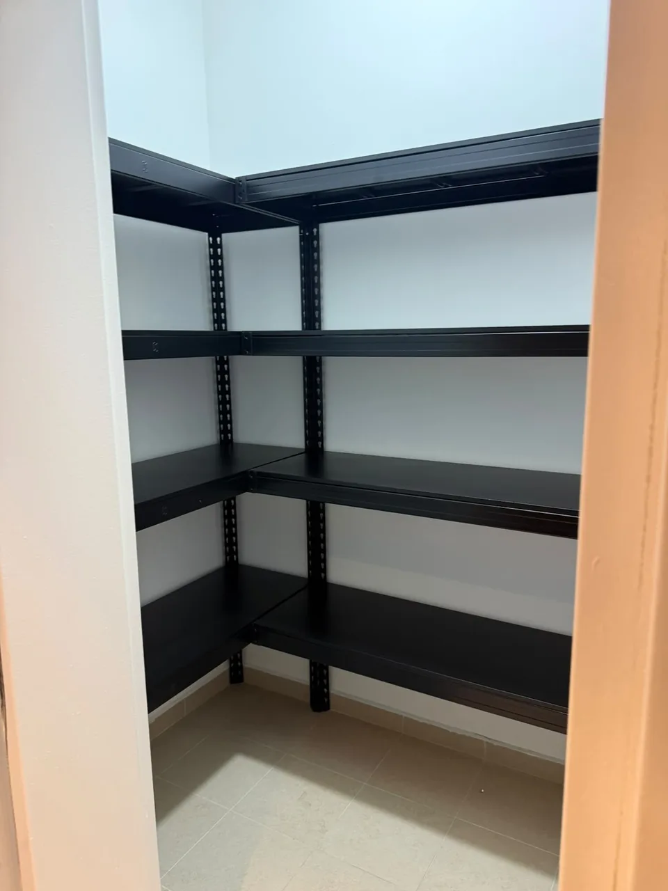 Black L-shaped shelving along two storeroom walls, viewed through a doorway